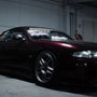 Dark red Nissan 200SX sports car with decals, parked indoors under garage lighting.