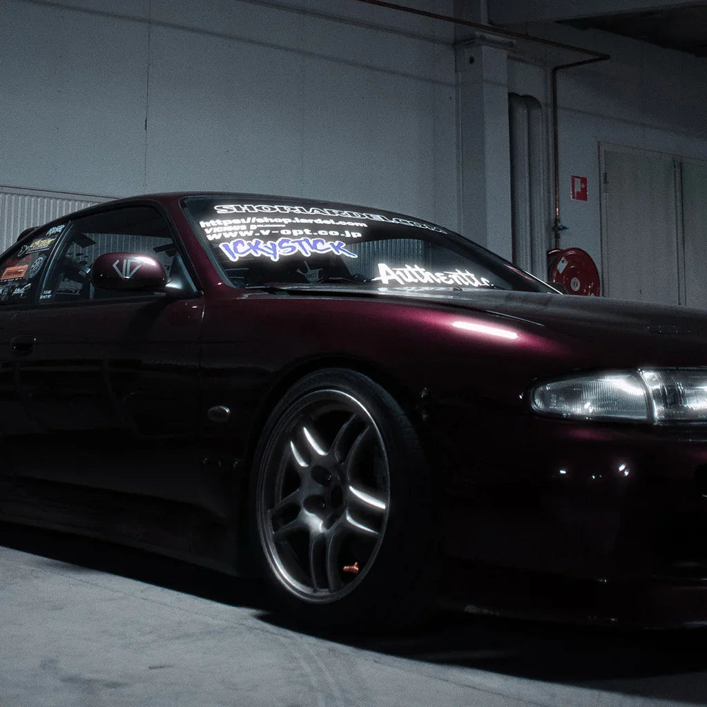 Dark red Nissan 200SX sports car with decals, parked indoors under garage lighting.