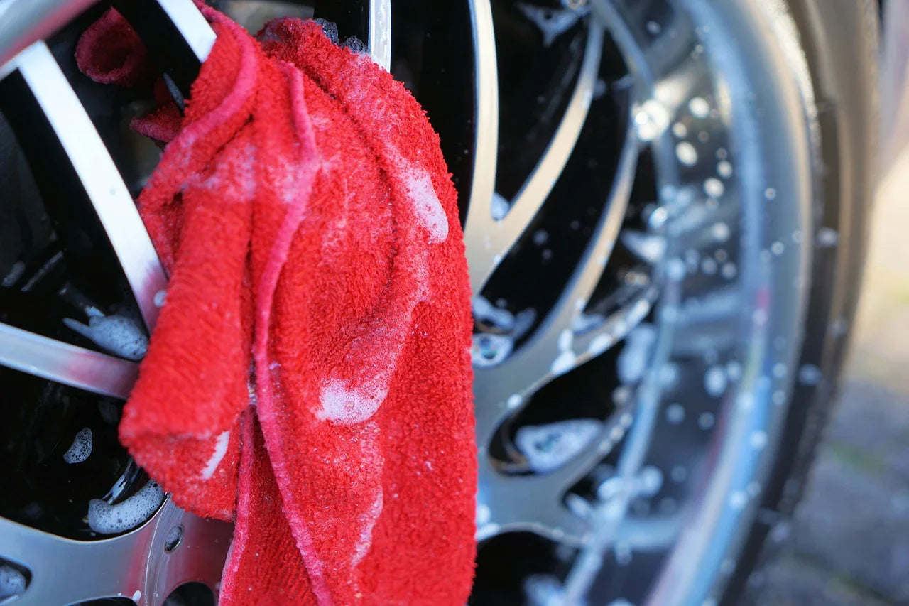 Red microfiber cloth with soap suds cleaning alloy car wheel, car care concept