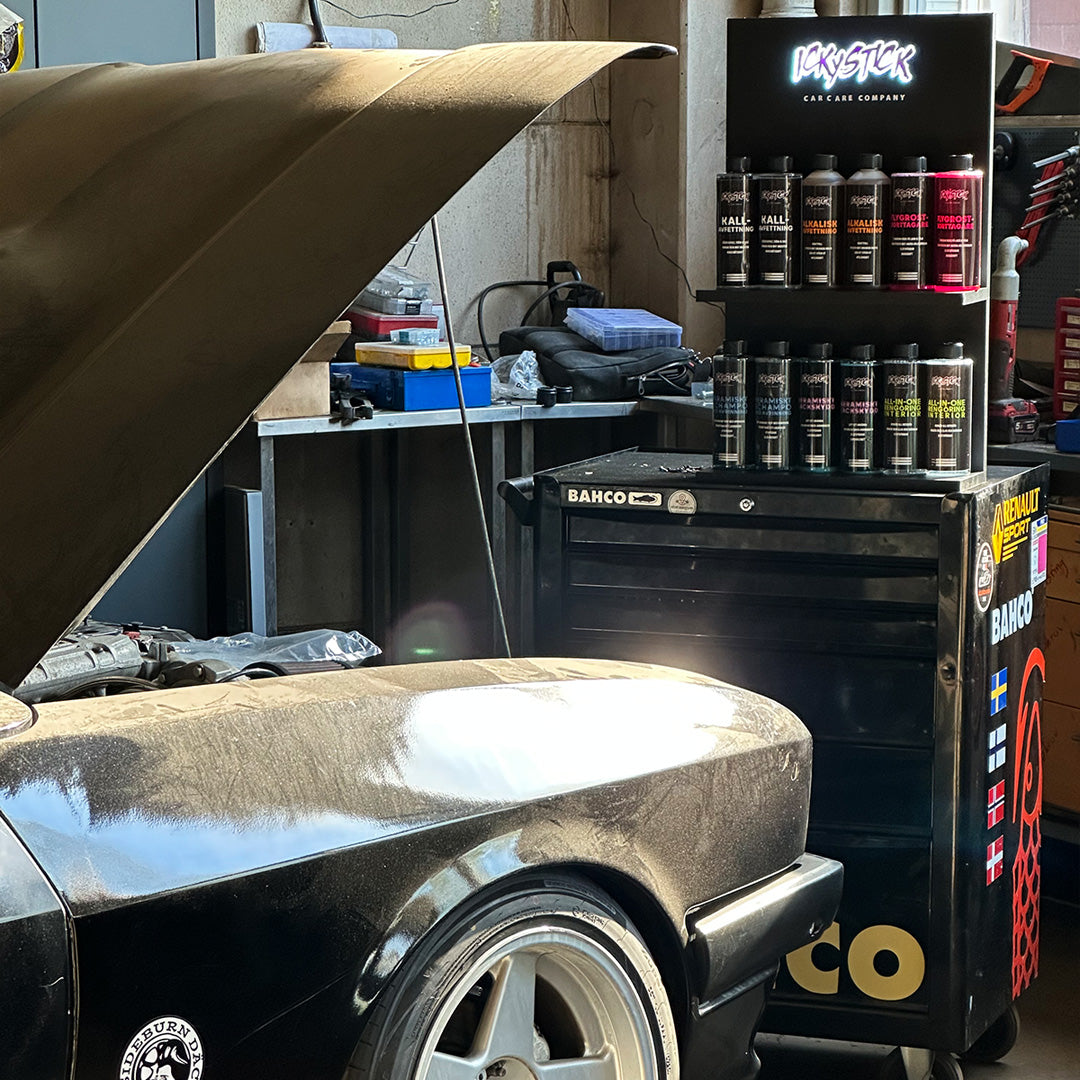 Car care products on display stand next to a black car with open hood in a garage